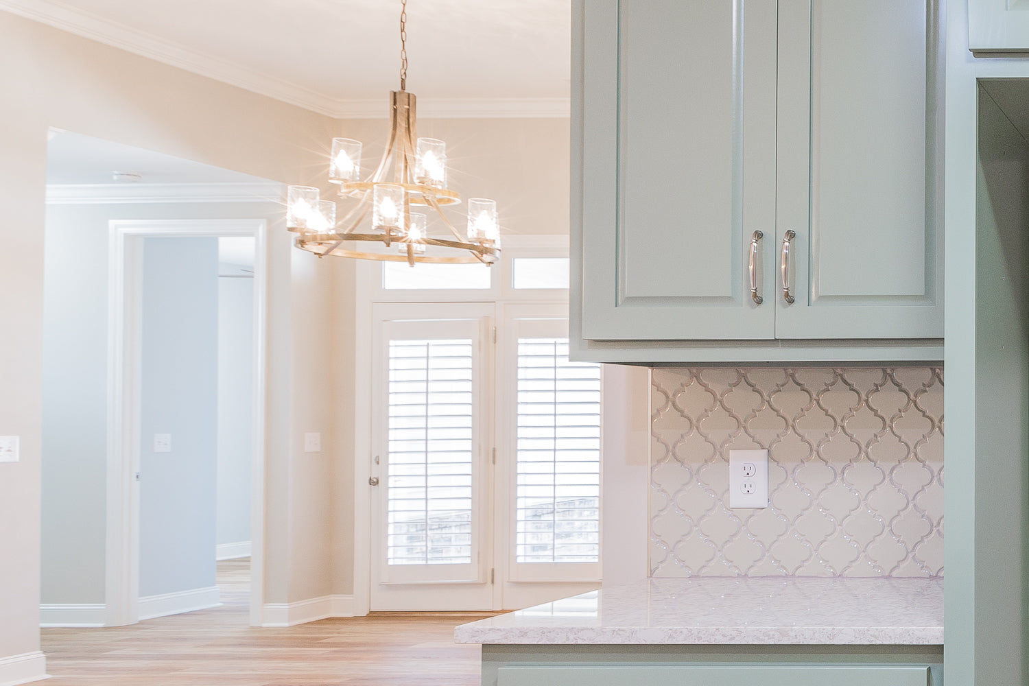 Modern kitchen with light green cabinets, white countertops, and a chandelier.