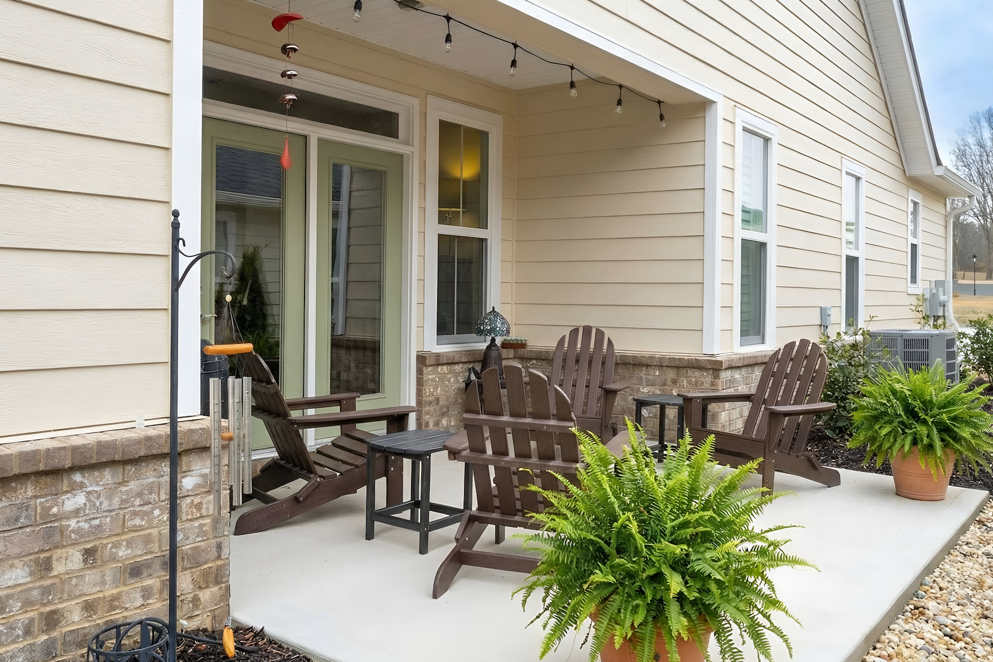 Outdoor patio area with wooden chairs, table, and potted plants on a house exterior.