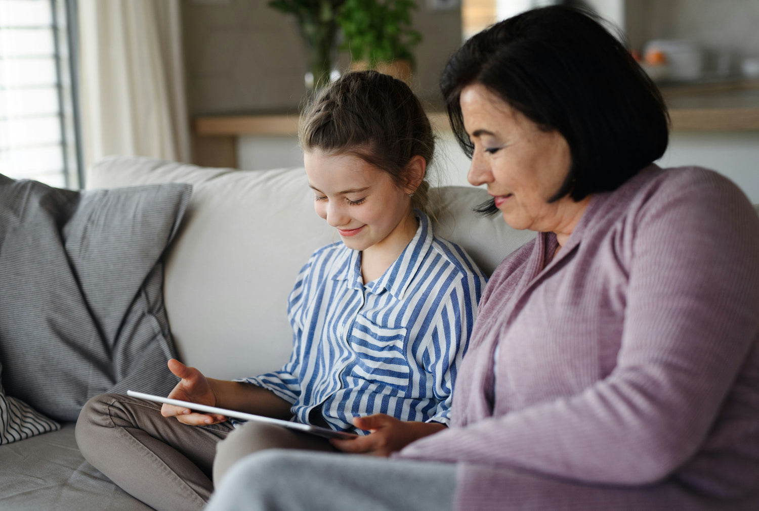 Woman and young girl sitting on a couch using a tablet together.